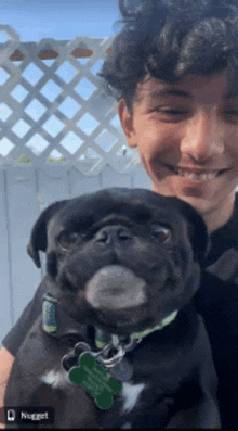 a man holding a black pug dog with a tag that says nugget on it