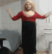 a man in a red top and black skirt is dancing in a room with his arms outstretched .