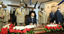 a man wearing a mask is signing a book in front of a table of flowers