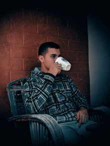 a man in a plaid shirt drinks from a cup that says t-shirt