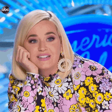 a woman wearing a floral shirt and earrings is sitting on a stage with her hand on her chin .