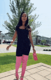 a woman in a black jumpsuit and pink over the knee boots is standing on a sidewalk .