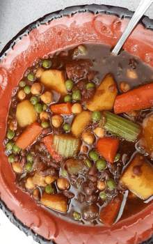 a bowl of stew with carrots peas and potatoes with a spoon in it