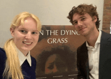 a man and a woman are posing for a picture in front of a poster for the dying grass