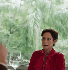 a woman in a red shirt is sitting at a table with a glass of water in front of her