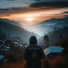 a person wearing a baptishurer hoodie stands in front of a foggy mountain range