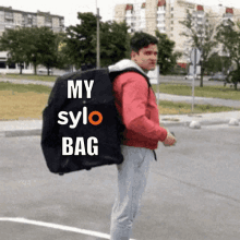 a man in a red jacket is carrying a large black bag that says my sylo bag