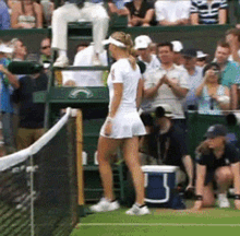 a woman stands on a tennis court in front of a crowd and a blue cooler with the letter b on it