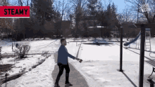 a man in a blue jacket is walking in the snow near a playground with a steamy sign above him