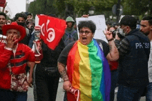 a woman is holding a rainbow flag and a sign while walking down a street with a crowd of people .