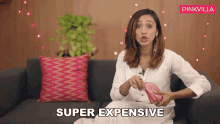 a woman is sitting on a couch and holding a pink purse and says super expensive