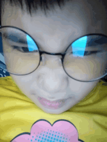 a young boy wearing glasses and a yellow shirt with a pink heart on it