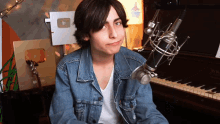 a young man in a denim jacket is sitting in front of a piano with a microphone attached to it