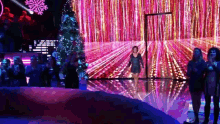 a woman is walking on a stage with a christmas tree in the background