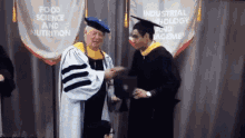 a man in a graduation cap and gown shakes hands with another man in front of a banner that says industrial physiology