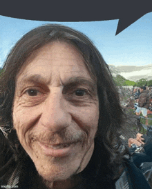 a man with long hair and a mustache is smiling in front of a crowd of people