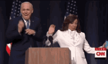 a man in a suit and tie is standing next to a woman in a white suit behind a podium that says cnn