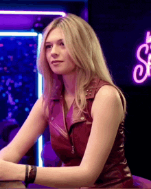 a woman in a red leather vest sits at a bar in front of a neon sign that says ' sf '