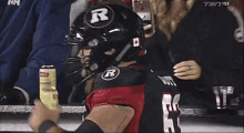 a football player in a red and black uniform is standing on a bench holding a can of soda .