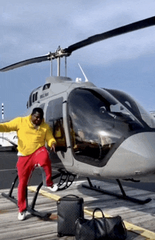 a man in a yellow sweatshirt stands in front of a helicopter that says ' helicopter ' on the side