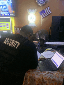 a man wearing a security vest is looking at a laptop