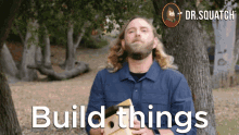 a man in a blue shirt is holding a piece of wood with the words build things written on it