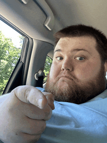 a man with a beard is sitting in a car pointing at the camera