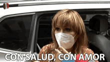 a woman wearing a face mask is sitting in a car and the words con salud con amor are above her