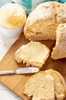 a loaf of bread is sitting on a wooden cutting board with butter on it