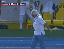 a man in a white shirt is walking on a blue track in front of a scoreboard that says game 0