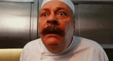 a man with a mustache and a chef 's hat is making a surprised face .