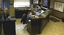 a man is sitting at a desk in an office with a map of the world on the wall behind him