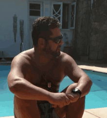 a shirtless man wearing sunglasses sits next to a pool