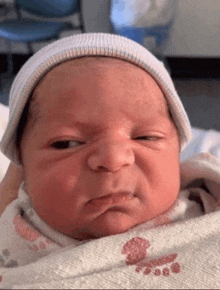 a newborn baby wearing a white hat is making a funny face .