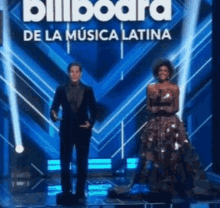 a man and a woman are standing on a stage in front of a sign that says billboard de la musica latina