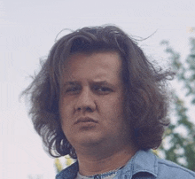 a man with long hair is wearing a blue shirt and looking at the camera