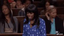 a woman in a blue polka dot shirt is sitting in a courtroom with other women .