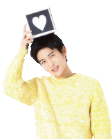 a young man in a yellow sweater is holding a heart shaped sign on his head