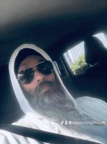 a man with a beard wearing sunglasses and a white hoodie is in a car