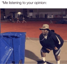 a man wearing headphones is listening to his opinion while standing next to a trash can .