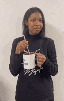 a woman is holding a cup of coffee and a spoon in her hand .