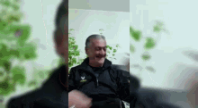 a man in a black jacket is sitting on a couch laughing .