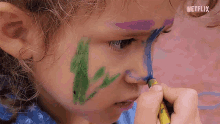 a little girl is painting her face with a crayon and the word netflix is visible in the corner .