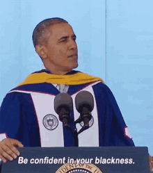 a man in a graduation cap and gown stands behind a podium that says " be confident in your blackness "