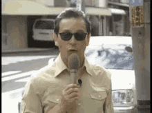 a man wearing sunglasses is holding a microphone in front of a car