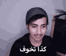 a young man wearing a black shirt and a beanie has arabic writing on his face