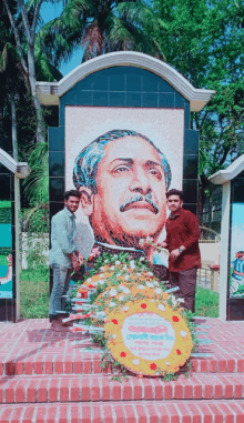 two men are standing in front of a statue of a man with a mustache