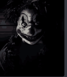 a scary clown with a crown on his head is smiling in the dark .