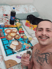 a man with a tattoo on his chest is smoking a cigarette in front of a table with food and a bottle of pepsi