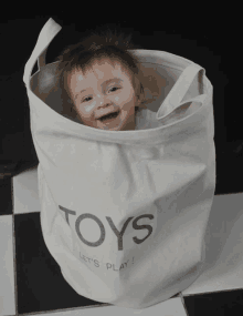 a baby is sitting in a laundry bag that says toys let 's play